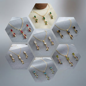 A collage of seven hexagonal panels showing gold-tone jewelry sets, each with a delicate branch-shaped pendant and matching earrings in different gemstone colors including red, green, black, white, purple, blue, and light green, displayed on soft gray fabric.