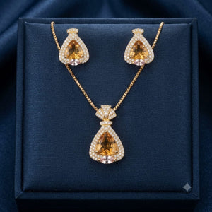 Gold-tone jewelry set with a teardrop pendant necklace and matching earrings, featuring large amber-orange center stones surrounded by clear rhinestones, displayed on a dark navy velvet jewelry box.
