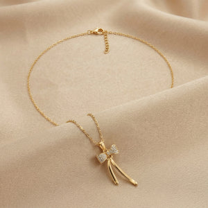 A delicate gold chain necklace with a bow pendant adorned with small clear stones, displayed on a soft beige fabric background.