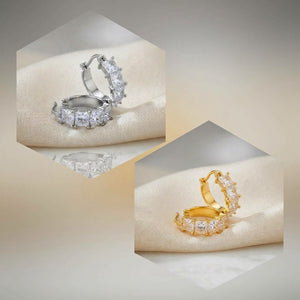 Two small hoop-style rings with clear rectangular stones, shown in silver and gold metal finishes on a soft cream fabric surface inside hexagonal frames.