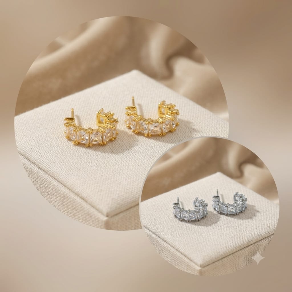 Two pairs of curved hoop earrings displayed on cream jewelry boxes, one in yellow gold and one in silver-tone metal, with a soft beige draped background.