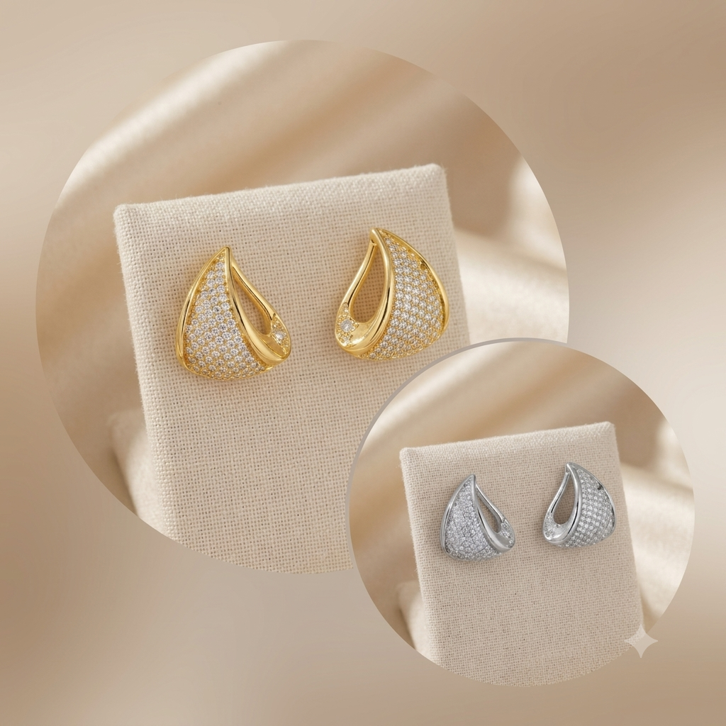 Teardrop-shaped stud earrings displayed on cream fabric jewelry stands, shown in two colorways: one gold-tone with pavé-set clear stones and one silver-tone with pavé-set clear stones, set against a warm beige satin background.