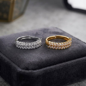 Two triple-row hoop rings, one silver-toned and one gold-toned, both set with clear marquise-cut stones, displayed on a dark gray velvet jewelry box.