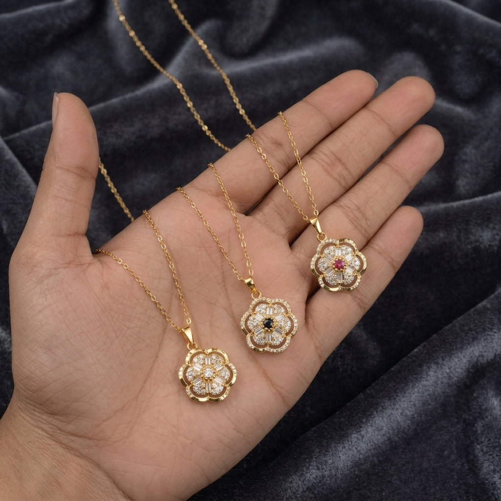 Three gold flower-shaped pendant necklaces with white stones and small colored center accents, displayed on an open hand over a dark velvet fabric background.