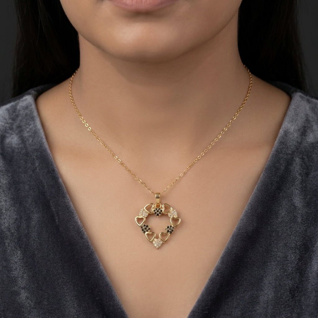 A close-up of a model wearing a delicate gold chain necklace with a heart-shaped pendant featuring small gold and silver floral details, paired with a dark gray velvet top.