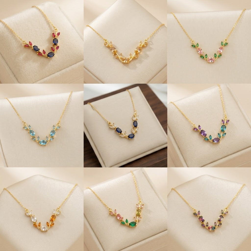 A 3x3 collage showing nine close-up views of gold-tone necklaces displayed on cream jewelry stands. Each necklace has a delicate leaf or vine motif with small multicolored gemstones in red, blue, green, pink, purple, orange, and clear stones.